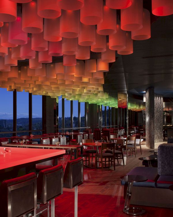 This image shows a modern restaurant or lounge with colorful ceiling lights, large windows, and contemporary furniture in a dimly lit atmosphere.